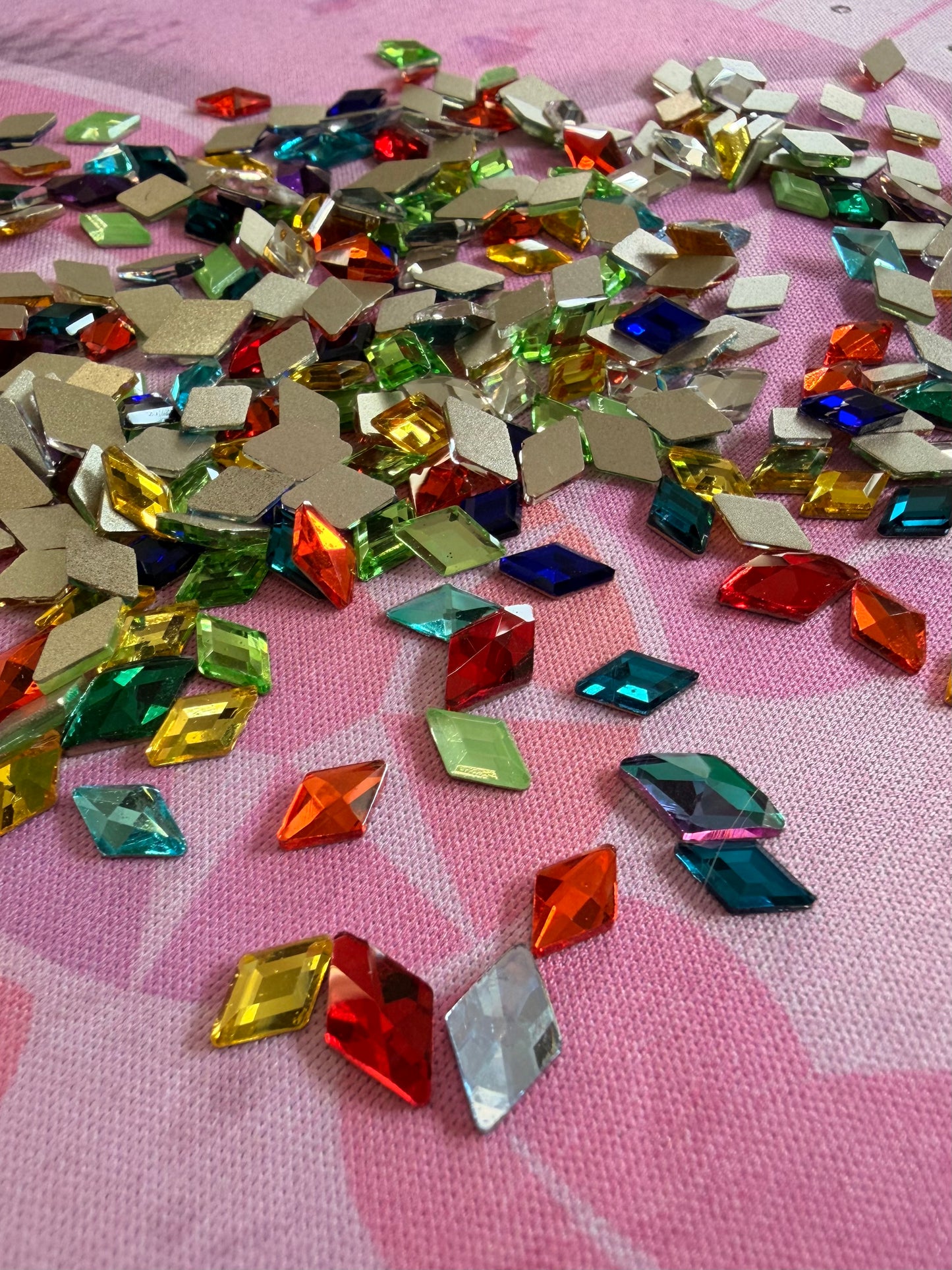 Multicolor diamond shaped rhinestones in red, green, blue, yellow and orange scattered on pink fabric