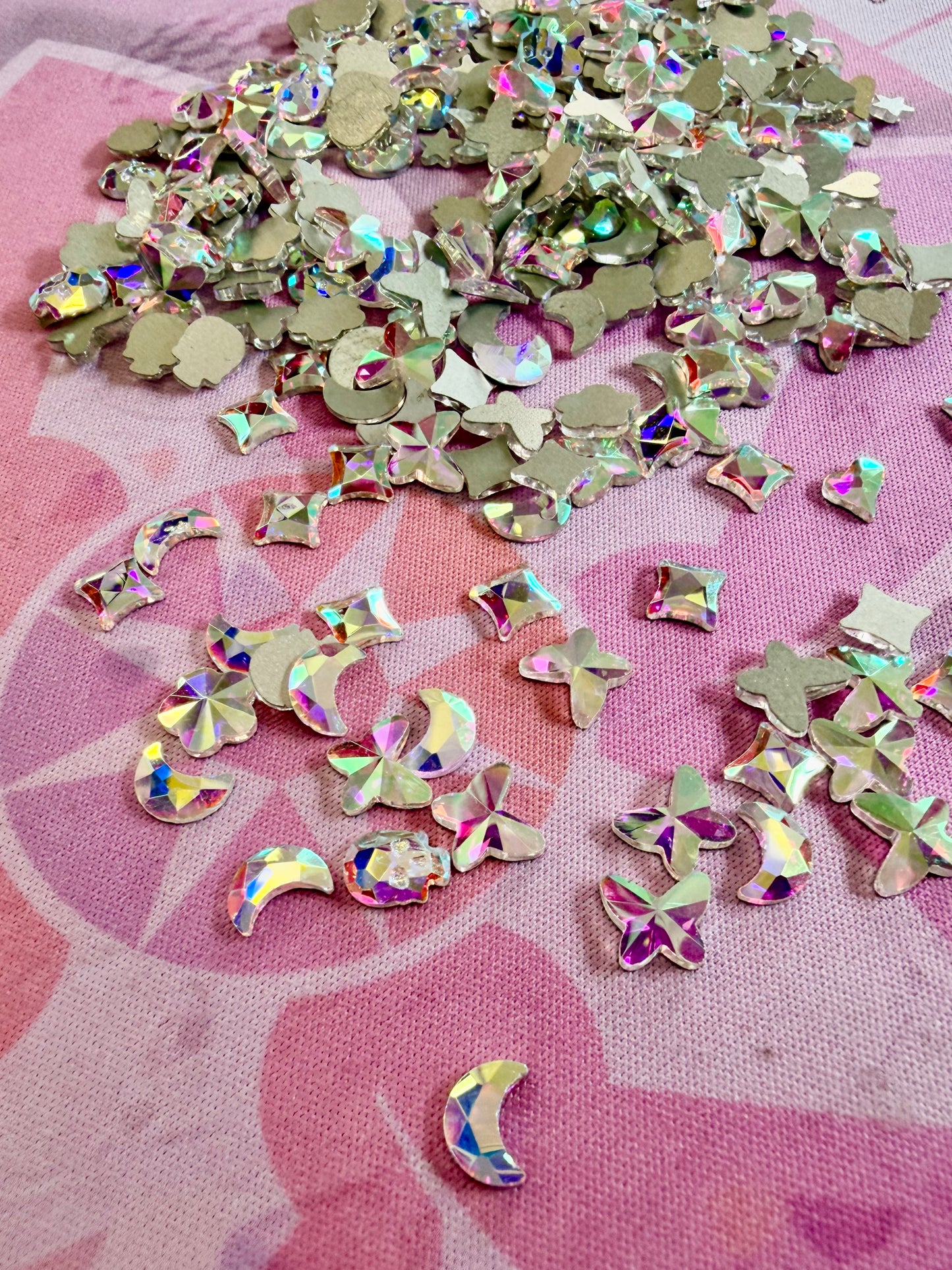 Crystal AB shaped rhinestones, moons, stars, butterflies and hearts, scattered on a pink mat