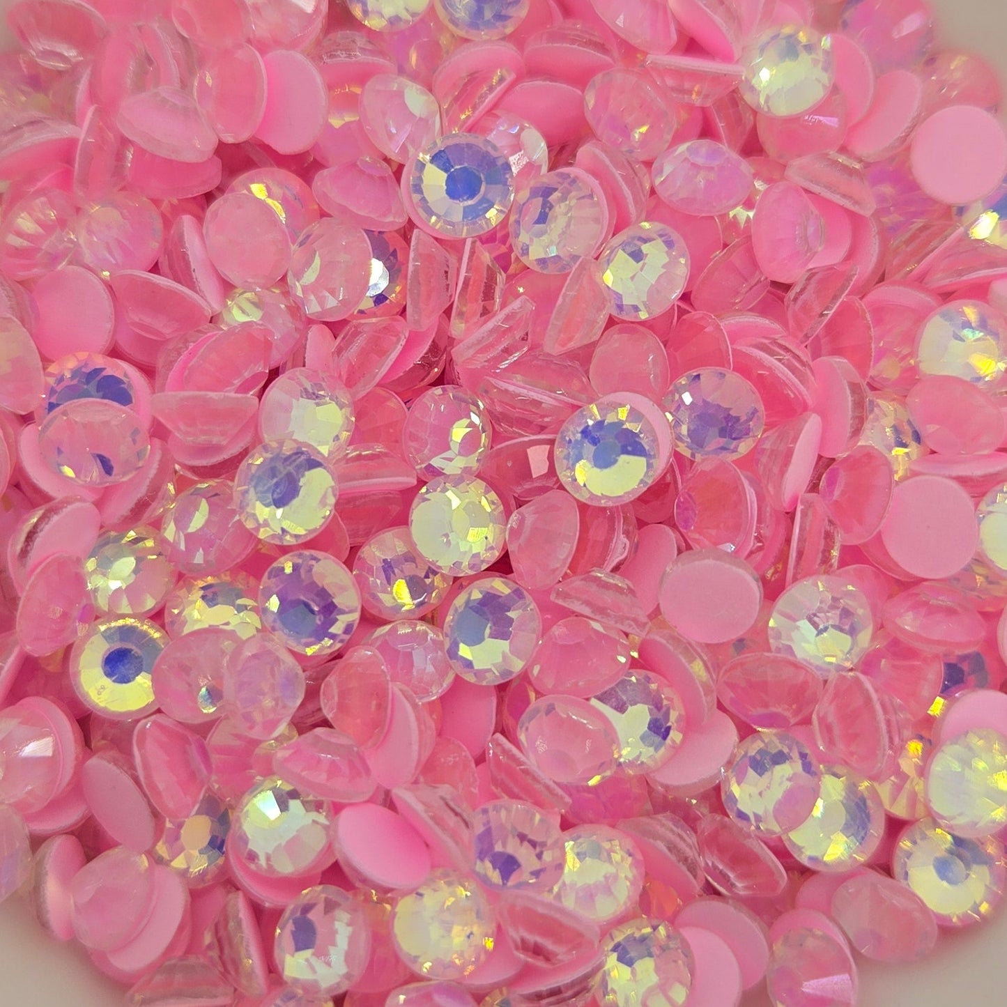 A collection of pink luminous opal flat back rhinestones in a white dish, with a blurred background.
