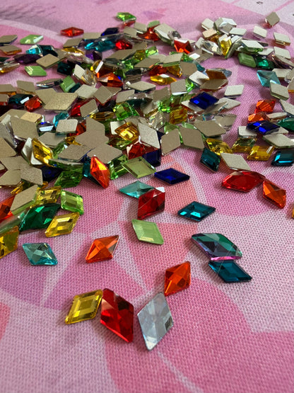 Multicolor diamond shaped rhinestones in red, green, blue, yellow and orange scattered on pink fabric