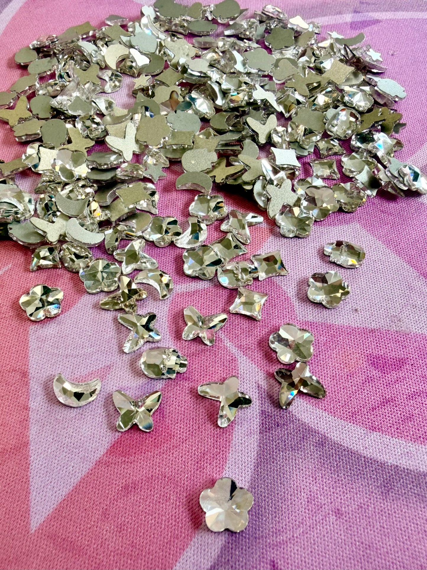 Clear crystal shaped rhinestones including butterflies, flowers, moons and hearts on a pink mat