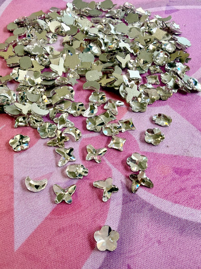 Clear crystal shaped rhinestones including butterflies, flowers, moons and hearts on a pink mat