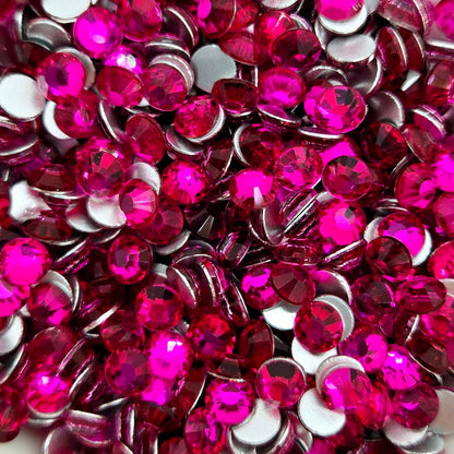 A collection of peach red flat back rhinestones arranged in a bowl, with a white dish and pink glittery background.