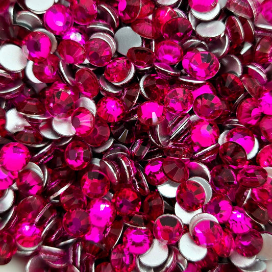 A collection of peach red flat back rhinestones arranged in a bowl, with a white dish and pink glittery background.