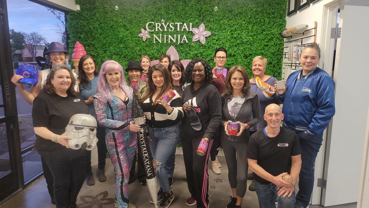 The Crystal Ninja and students holding their blinged projects in front of the CrystalNinja logo wall with a giant Crystal Katana