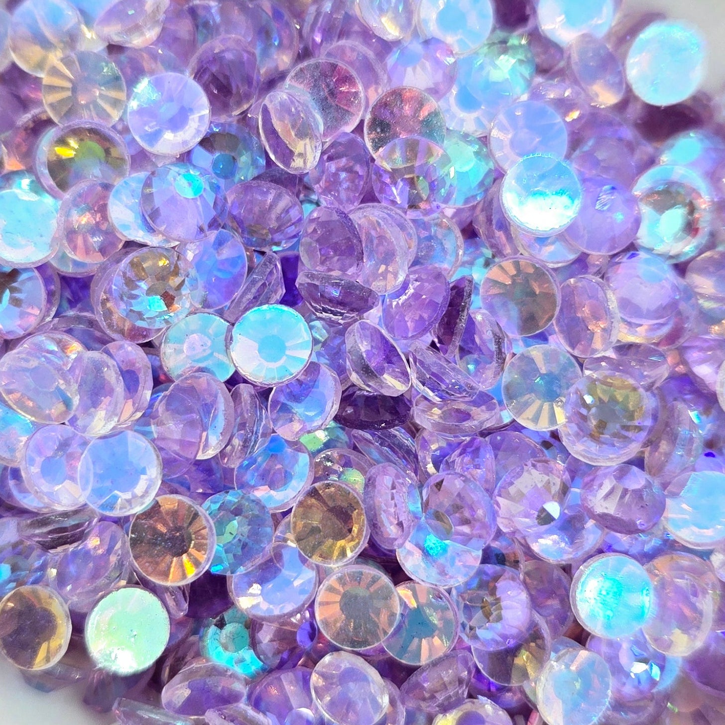 A collection of light amethyst colored rhinestones with a flat back, displayed in a white dish against a speckled background.