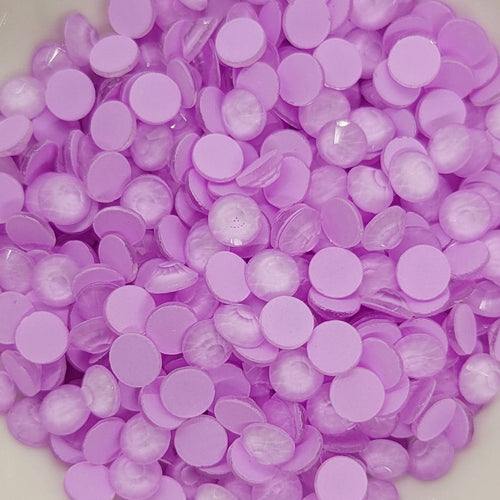 A bowl of luminous neon purple glass rhinestones on a white surface, with a blurred background.