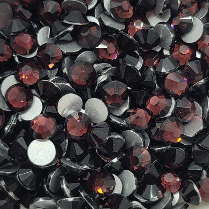 A bowl of purple and black glass rhinestones on a floral-patterned surface.