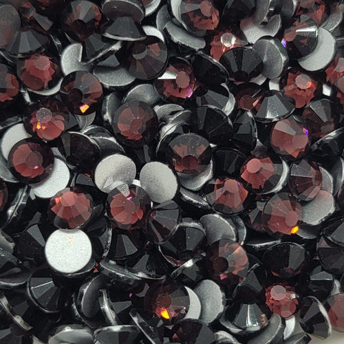 A bowl of purple and black glass rhinestones on a floral-patterned surface.