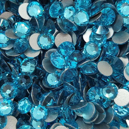 A bowl of aqua blue glass rhinestones with flatbacks, intended for crafting and jewelry making.