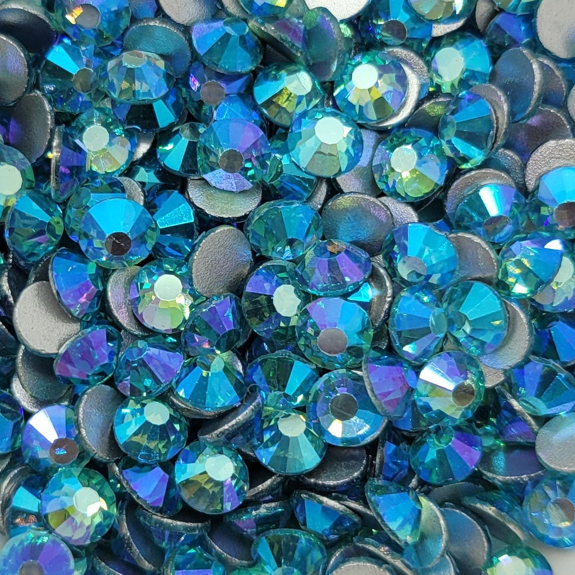 A bowl of blue and aqua colored glass rhinestones with a shimmering, iridescent finish.