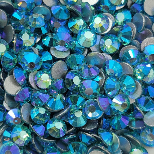 A bowl of blue and aqua colored glass rhinestones with a shimmering, iridescent finish.
