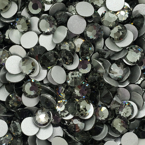 A bowl filled with black diamond glass rhinestones with flatbacks, displayed on a surface with a floral pattern.