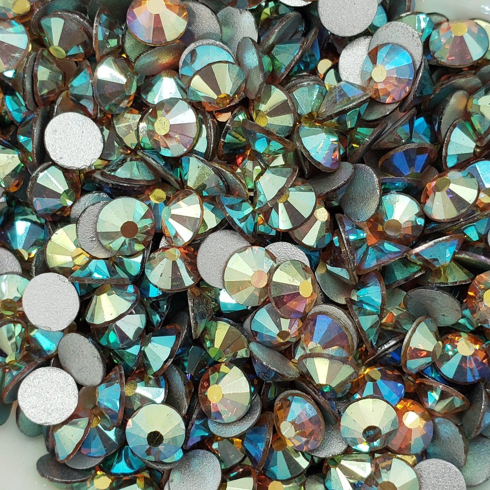 A bowl full of green and gold flatback rhinestones with a sparkling appearance.