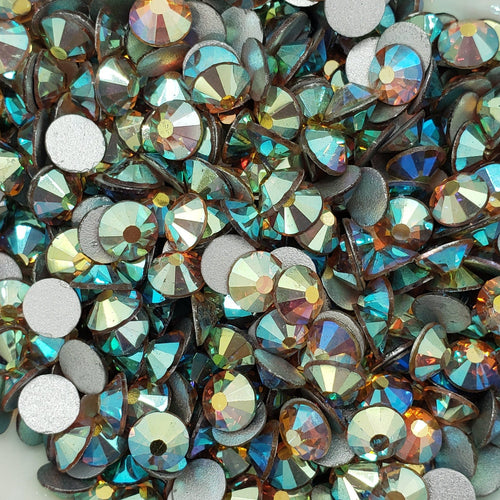 A bowl full of green and gold flatback rhinestones with a sparkling appearance.