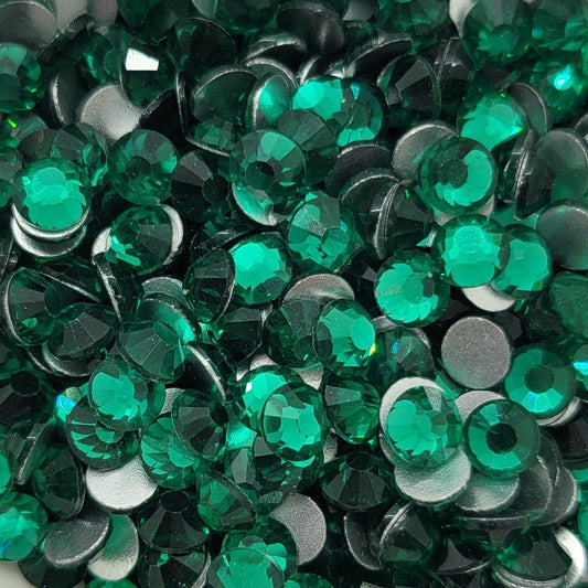 A bowl filled with green round glass rhinestones with a shiny finish, placed on a surface with a floral pattern.