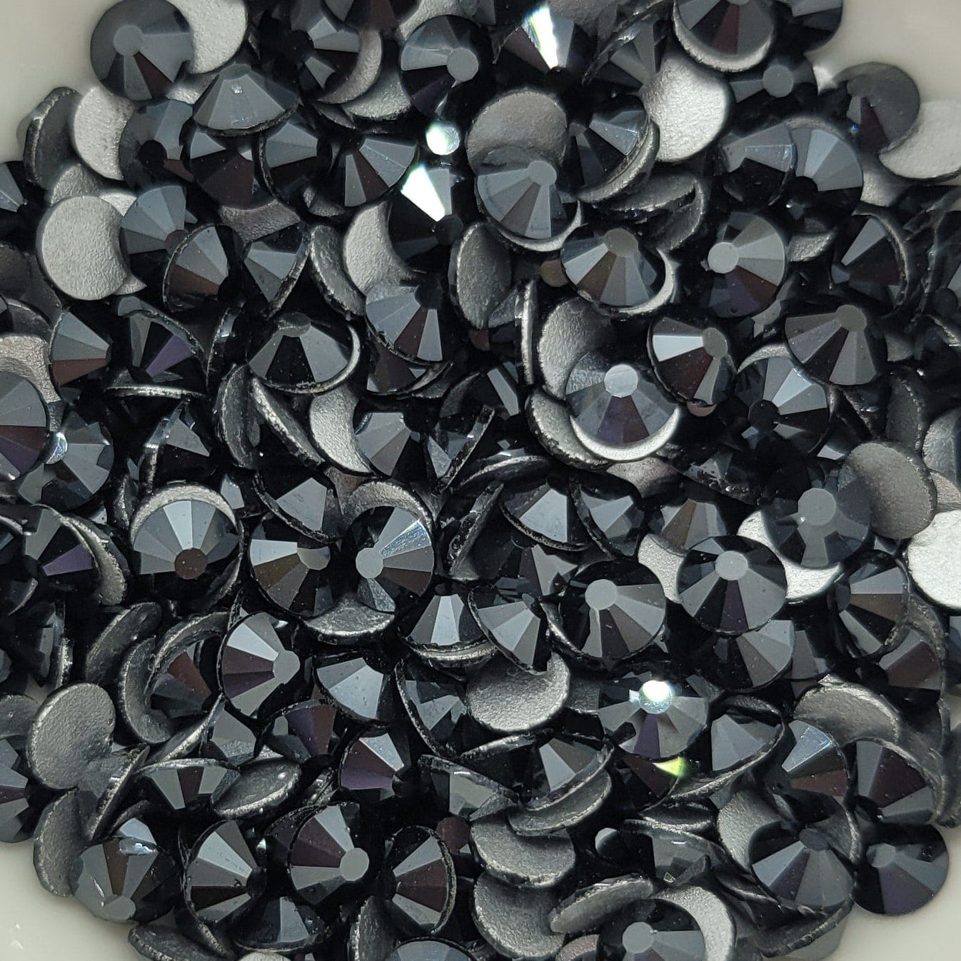 A bowl filled with black and gray glass rhinestones on a patterned background.