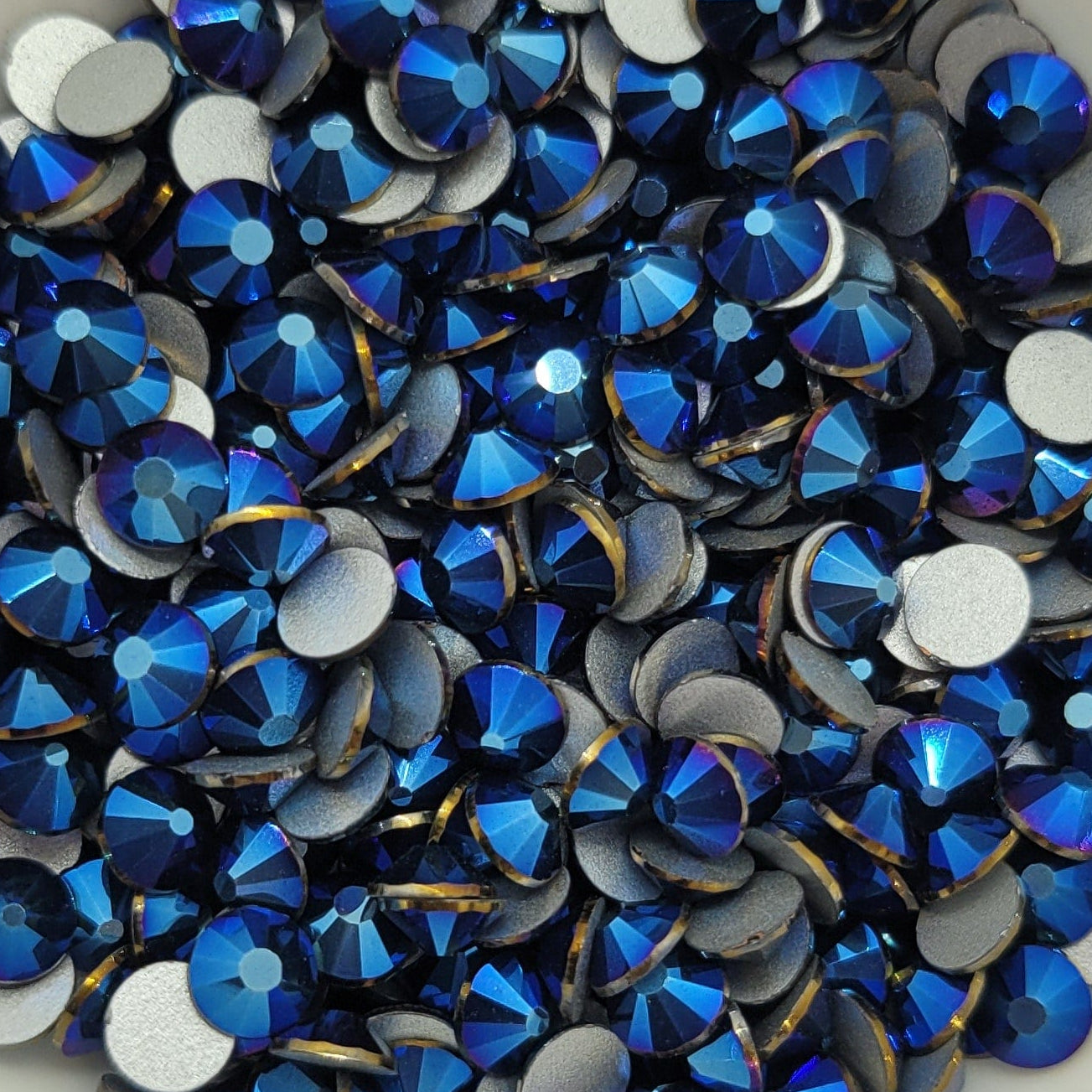 A bowl filled with metallic blue kira kira glass rhinestones on a floral patterned surface.