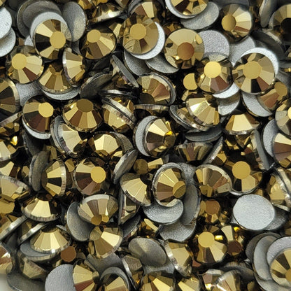 A white bowl filled with metallic gold Kirakira glass rhinestones on a floral patterned surface.