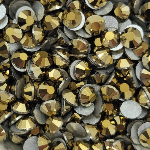 A white bowl filled with metallic gold Kirakira glass rhinestones on a floral patterned surface.