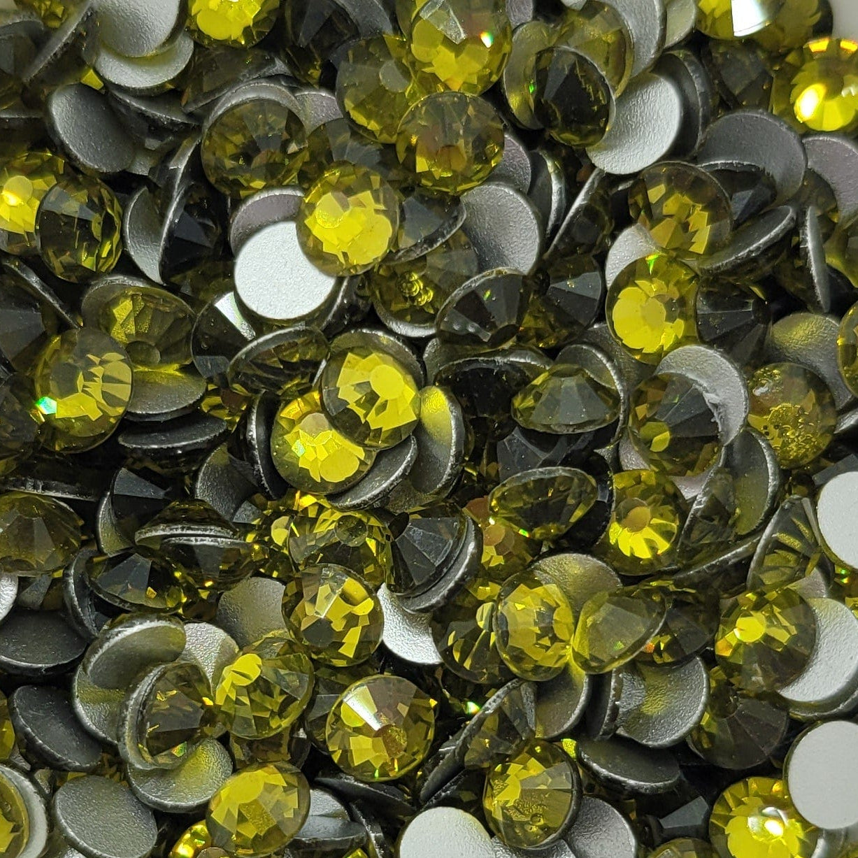 A bowl filled with yellow and clear round rhinestones on a floral patterned background.
