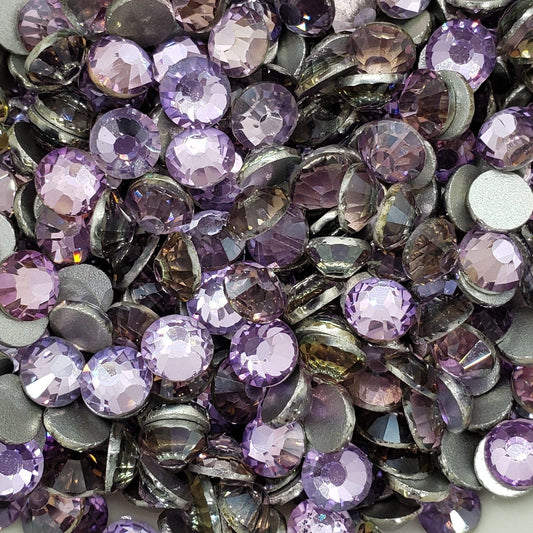 A collection of pink purple KiraKira glass rhinestones scattered on a white surface.