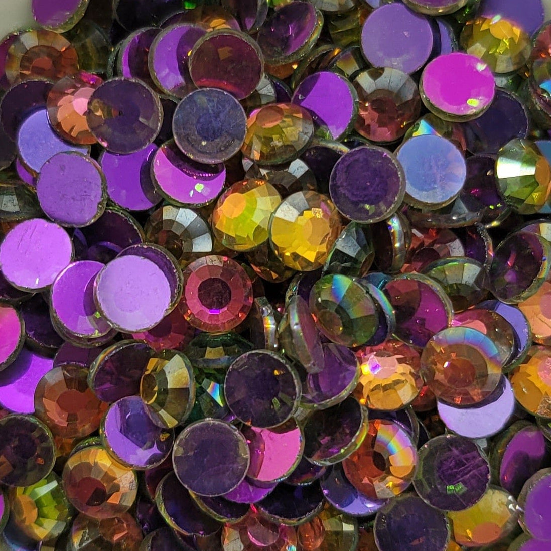 A bowl of multicolored round rhinestones with a reflective surface, on a patterned background.