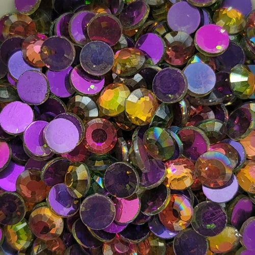 A bowl of multicolored round rhinestones with a reflective surface, on a patterned background.