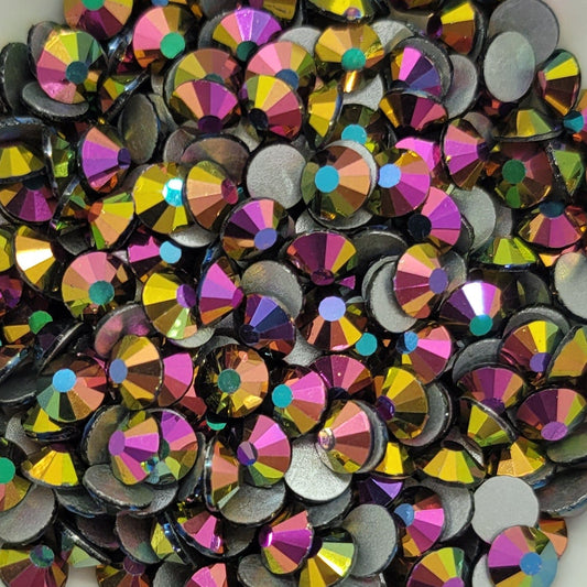 A bowl of multicolored glass rhinestones with a reflective iridescent finish on a floral patterned surface.