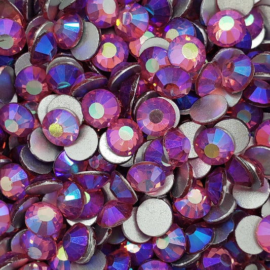 A dish of multicolored glass rhinestones with an iridescent finish, primarily in purple hues.