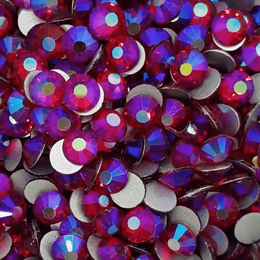 A collection of Siam Redish AB glass rhinestones with red and blue reflections, intended for crafting and gluing onto projects.