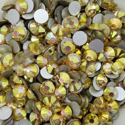 A collection of sunny gold colored flatback rhinestones arranged in a fan shape on a white surface.