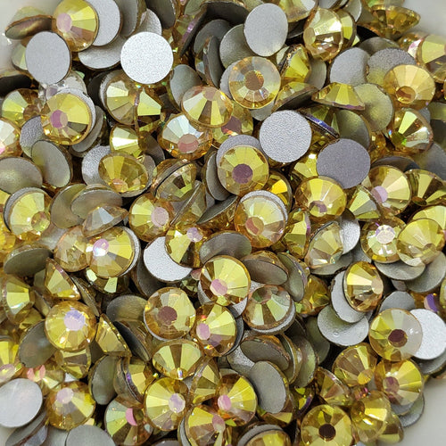 A collection of sunny gold colored flatback rhinestones arranged in a fan shape on a white surface.