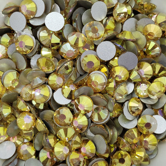 A collection of sunny gold colored flatback rhinestones arranged in a fan shape on a white surface.
