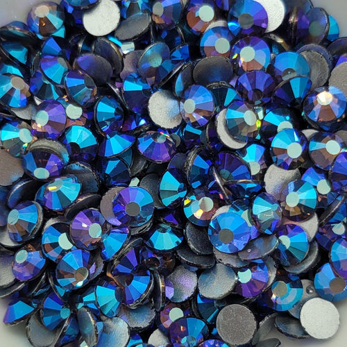 A dish filled with blue and purple glass rhinestones, intended for use in crafting and embellishing.