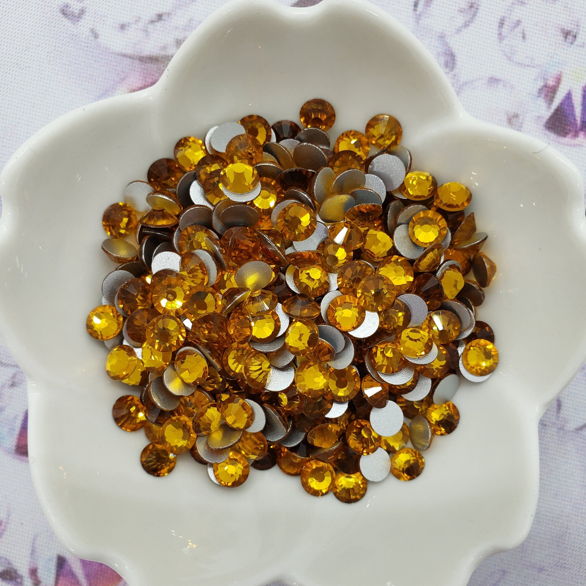 A dish containing amber-colored glass rhinestones on a patterned background.