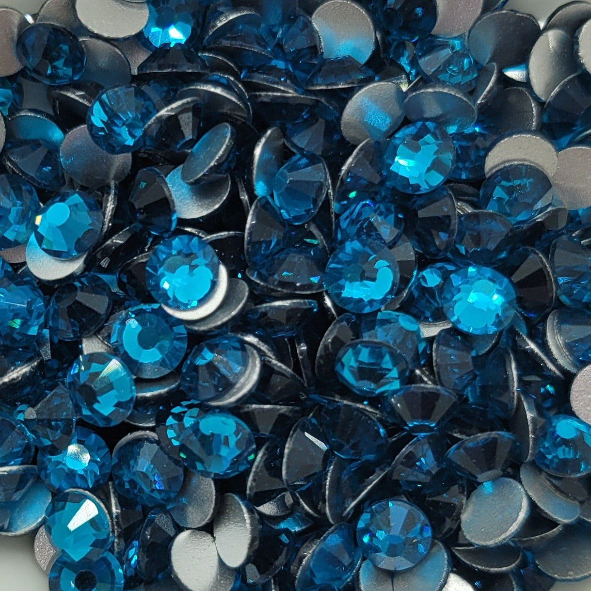 A white bowl filled with blue and clear glass rhinestones on a patterned surface.