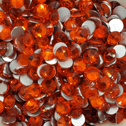 A bowl filled with orange flatback rhinestones on a floral patterned surface.