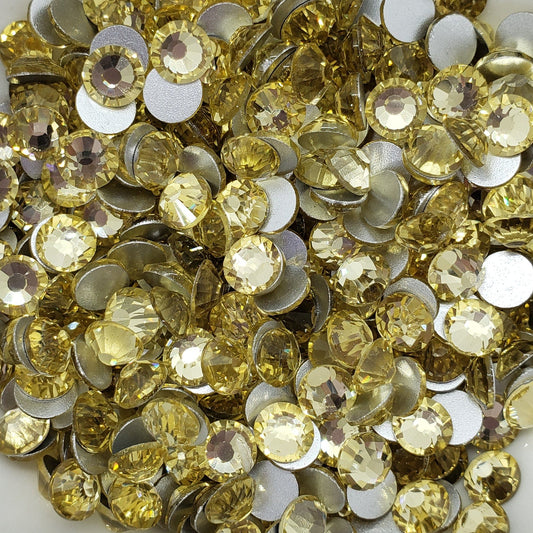 A collection of yellow glass flatback rhinestones arranged in a decorative pattern on a white dish with a floral background.