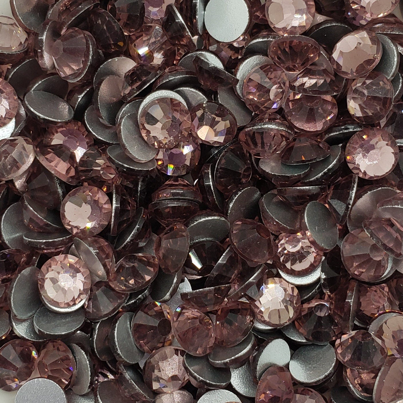 A collection of light amethyst colored glass rhinestones arranged in a decorative pattern on a white, scallop-edged plate.