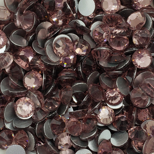 A collection of light amethyst colored glass rhinestones arranged in a decorative pattern on a white, scallop-edged plate.