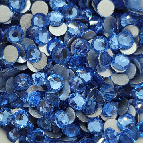 A dish containing multiple blue KiraKira glass rhinestones, placed on a white surface with a blurred background.
